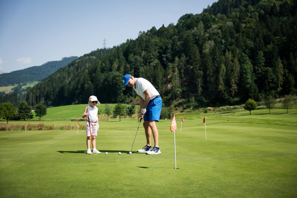 Ein Golflehrer zeigt der jungen Anfängerin das Putting am Grün